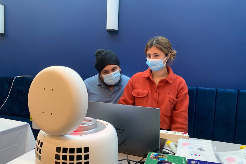 Two people in face masks examining a round piece of machinery which processes COVID-19 swabs