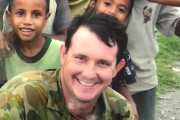 Young smiling solider surrounded by group of local children in East Timor, looking happy.