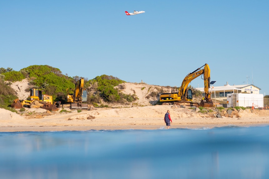 Machinery and a solitary walker on an Adelaide beach.