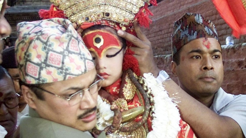The child goddess in elaborate dress sleeps in a man's arms while another man holds up her headdress