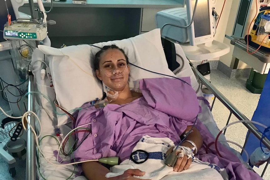 Woman sits looking sick in hospital bed with tubes. 