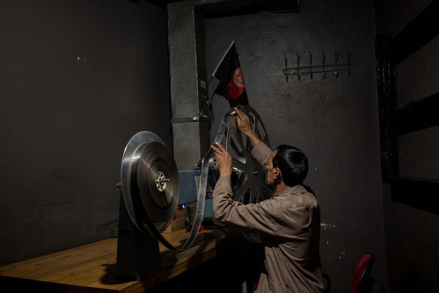 a man plays back a film roll in a room in the ariana cinema in kabul
