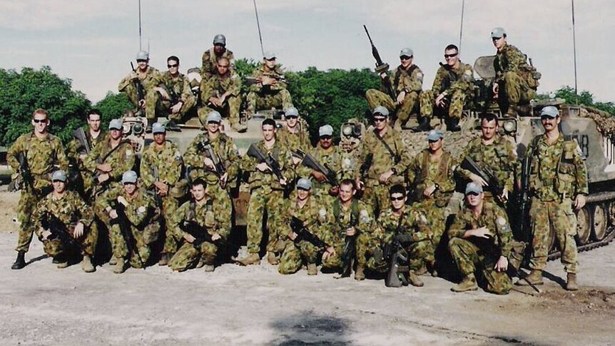 A platoon of Australian soldiers pose for a photo in front of tanks.