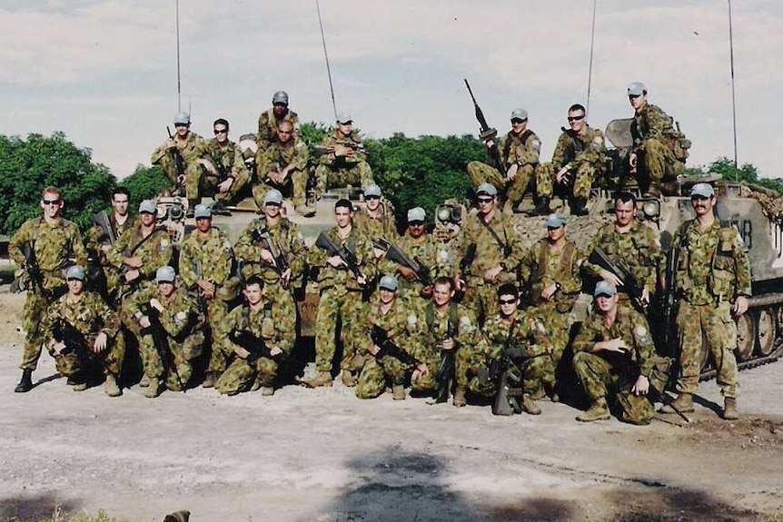 A platoon of Australian soldiers pose for a photo in front of tanks.