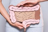 A woman holds a paper cut-out of a large intestine in front of her abdomen.