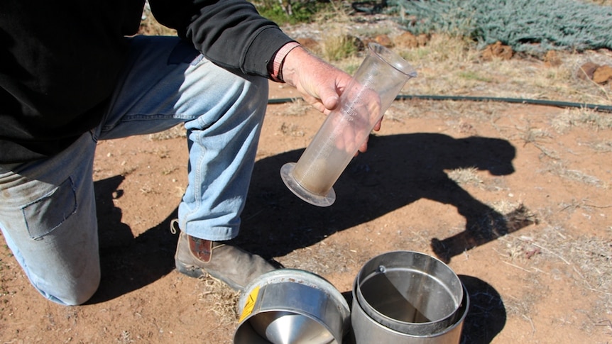 A farmer checking an empty rain gauge