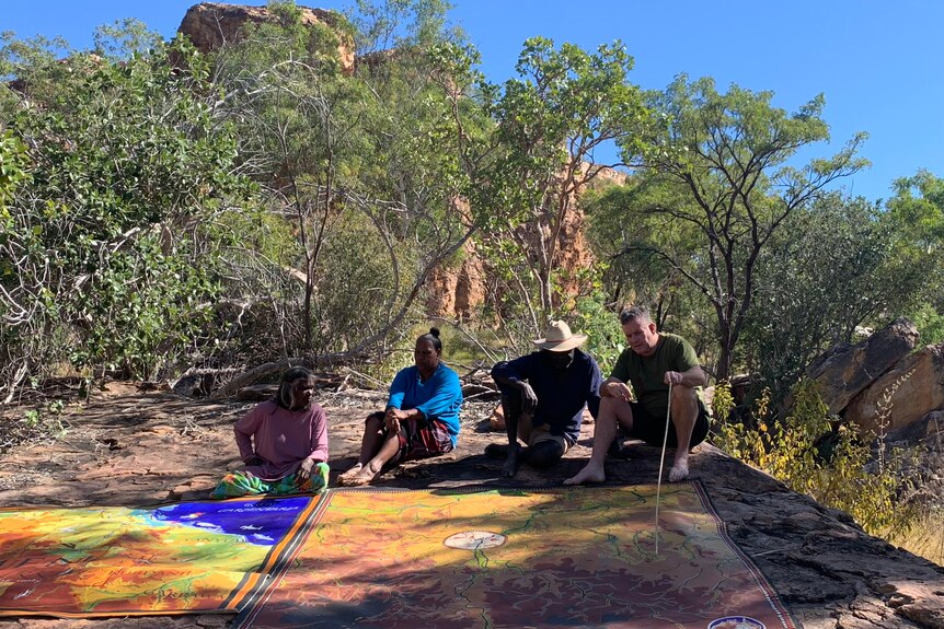 Four people sit together looking at a large colourful map on the ground