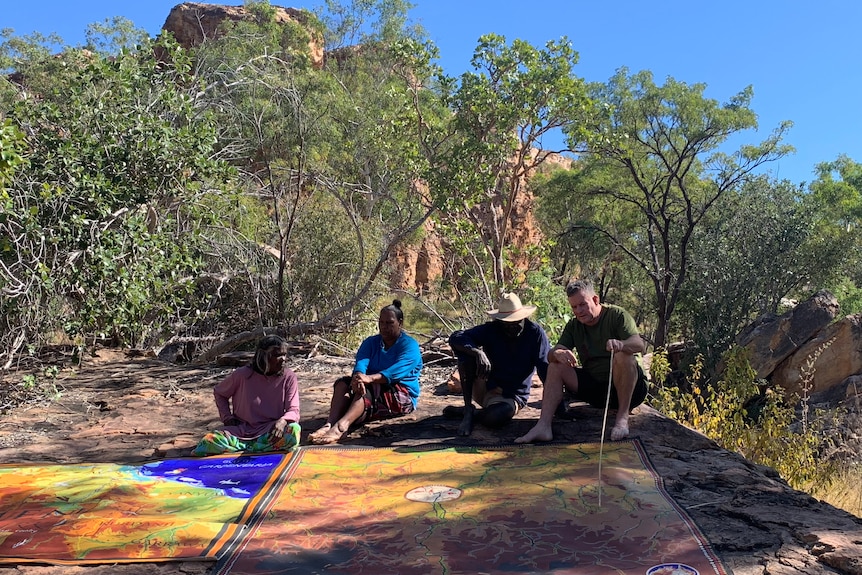 Four people sit together looking at a large colourful map on the ground