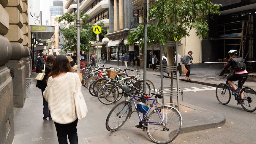 A narrow, busy street with period buildings, parked bicycles and hurried pedestrians.