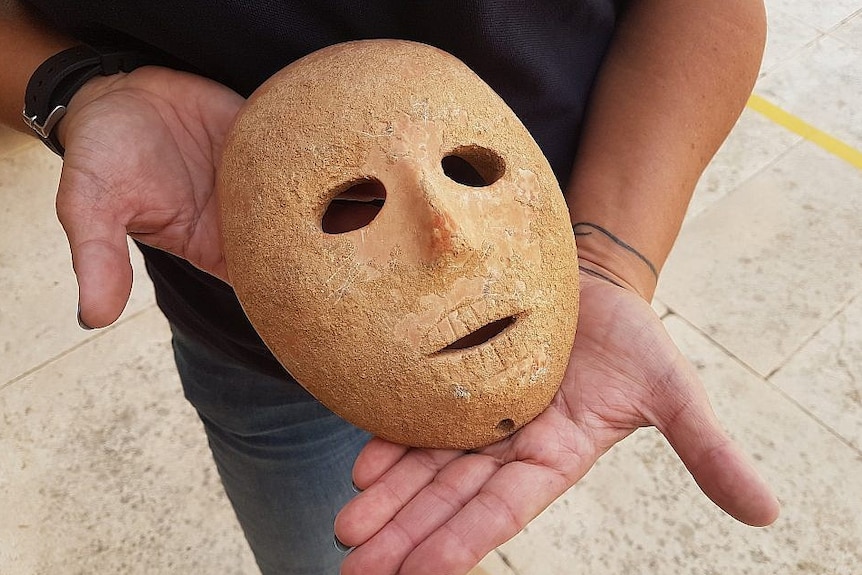 A stone mask is held in a person's hands