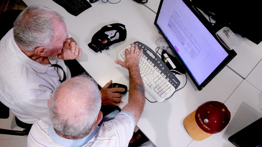 Two older men use a computer together.