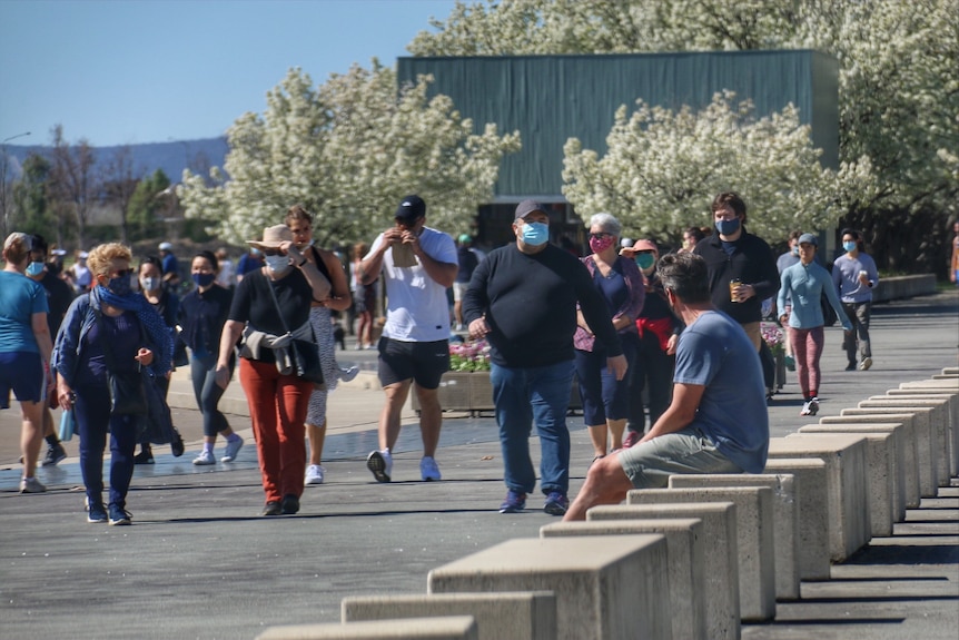 Big group of people walking on a sunny day wearing masks outside