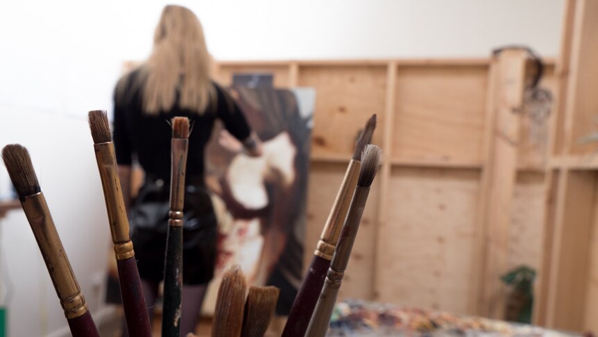 Ellie Kammer works on her endometriosis painting, with a jar of paintbrushes in the foreground.
