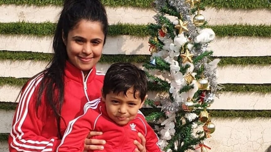 A woman with a little boy on her lap, both in matching red Adidas tracksuits 
