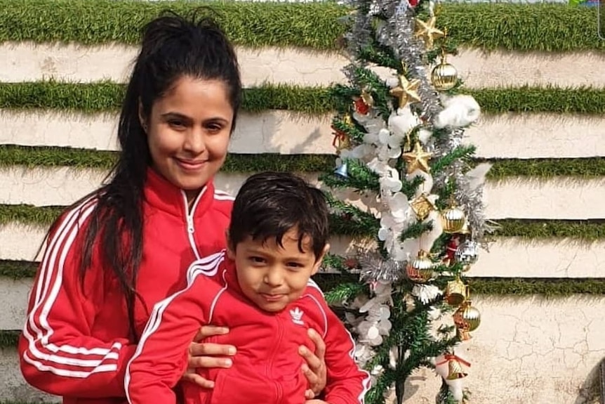 A woman with a little boy on her lap, both in matching red Adidas tracksuits 
