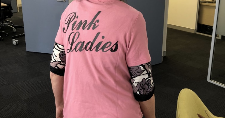 A woman whose face is not seen wears a bright shirt decorated with the words Pink Ladies.