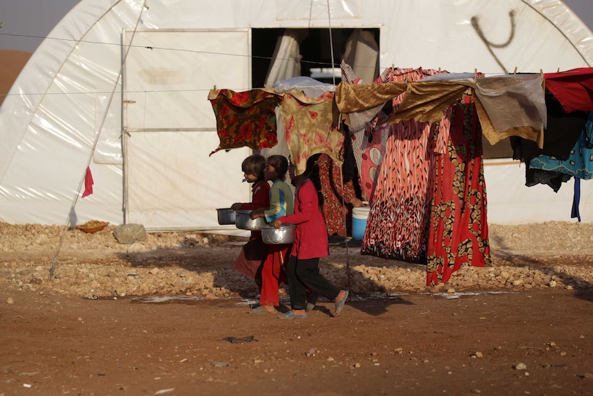 Young girls in Aleppo carry pots of food past a clothesline.