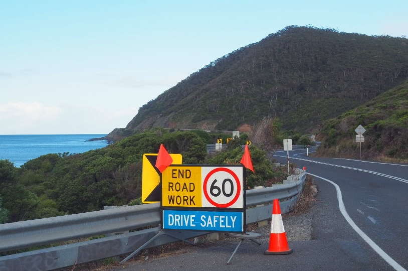A sign reading 'End road work, drive safely' sits on a road beside the ocean.