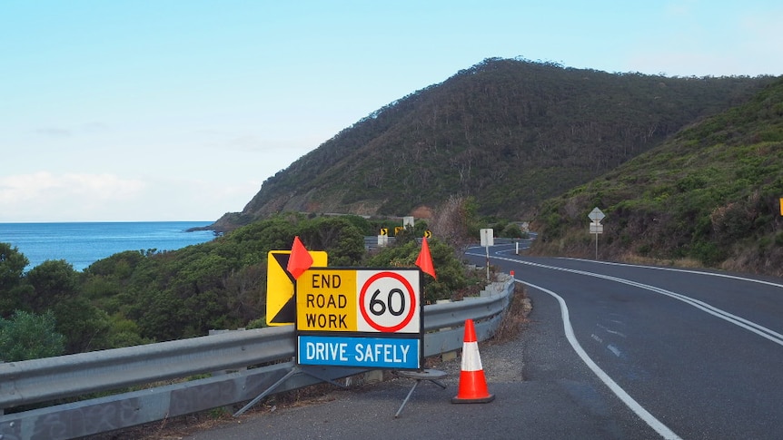 A sign reading 'End road work, drive safely' sits on a road beside the ocean.