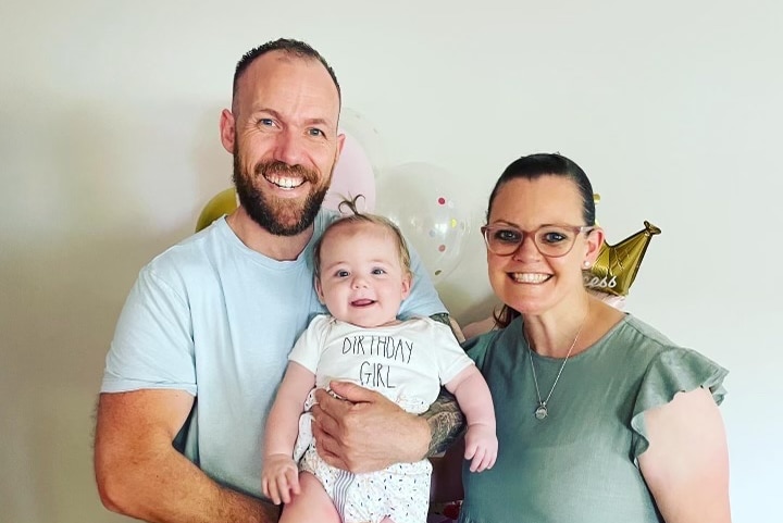 A man and a woman smiling while holding a one-year-old