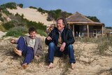Geoffrey Rush sits next to a boy on the sand during the filming of Storm Boy.