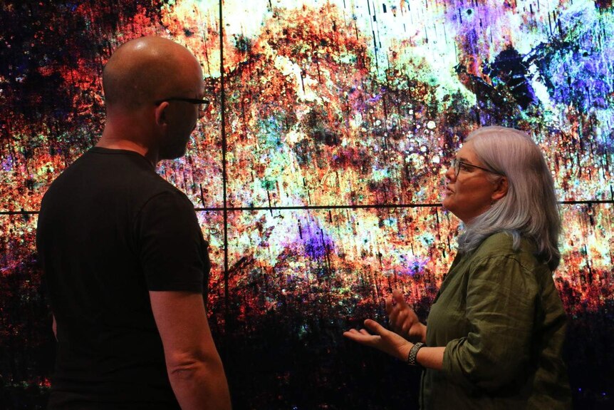 Two people stand in front of a colourful image of the surface of Mars.