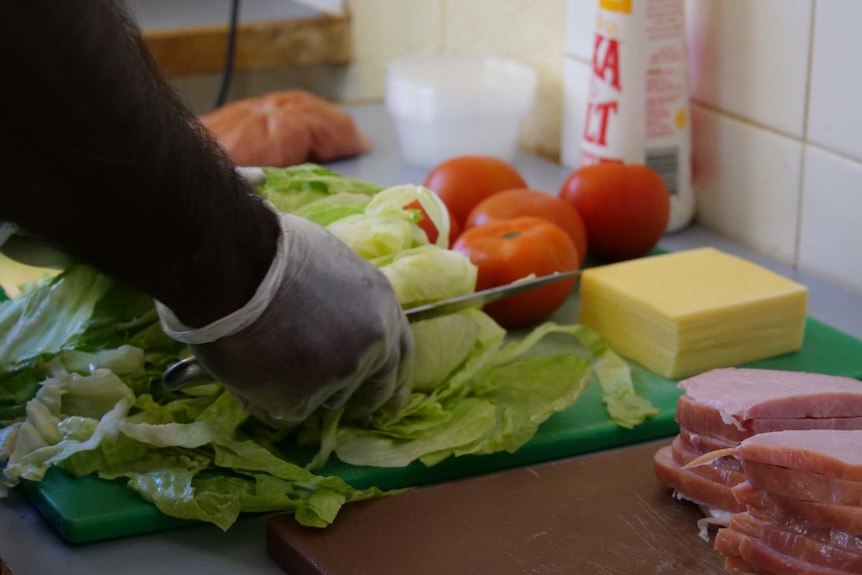 Close up on lettuce and tomato being cut up on a chopping board for ham sandwiches