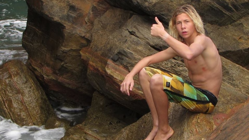 Cooper Allen giving thumbs up to camera at a rock ledge at beach.
