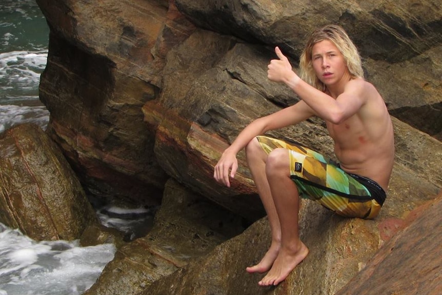 Cooper Allen giving thumbs up to camera at a rock ledge at beach.