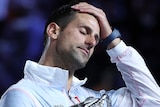 Novak Djokovic touches his forehead as he holds the Australian Open trophy.