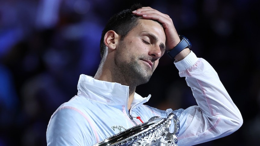 Novak Djokovic touches his forehead as he holds the Australian Open trophy.
