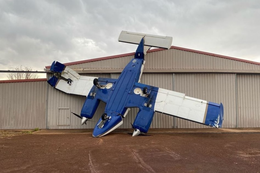 Light aircraft standing upside down against airport shed