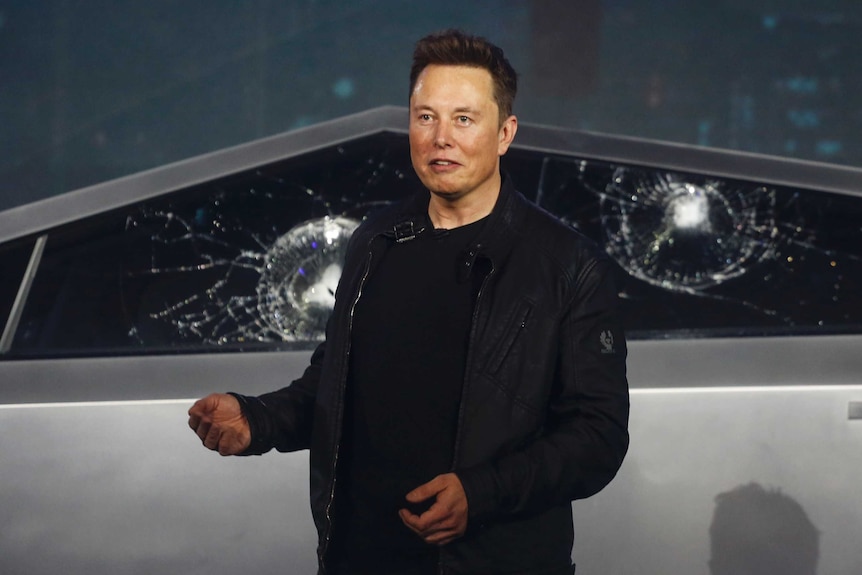 Elon Musk stands infront of the smashed windows of a Cybertruck