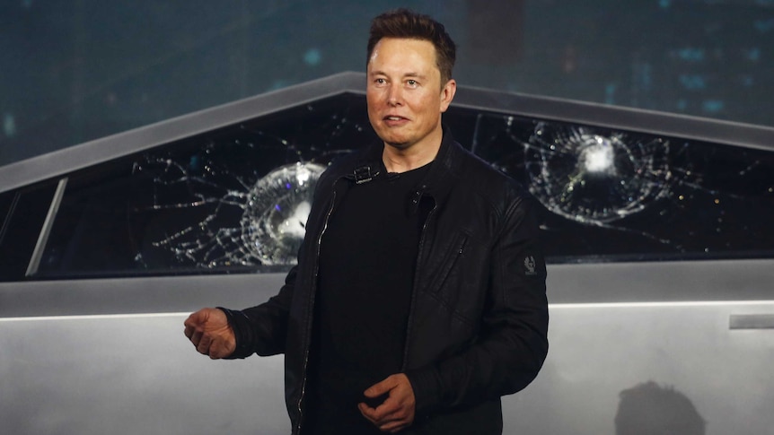 Elon Musk stands infront of the smashed windows of a Cybertruck