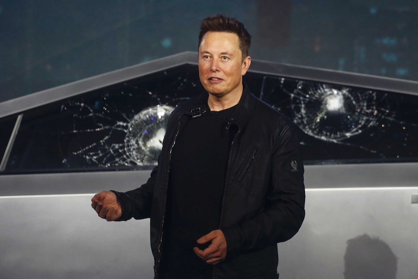 Elon Musk stands in front of the smashed windows of a Cybertruck