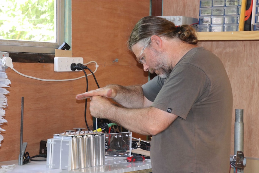 Chris Jones from the Electric Vehicle Association WA wears safety glasses as he uses hand tools in a workshop.