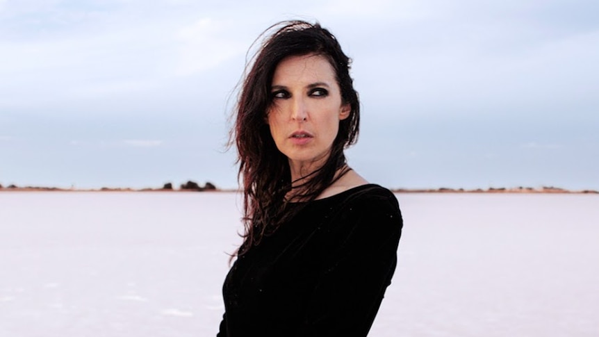 Singer Adalita in a black outfit, standing on a cold looking wind-swept beach