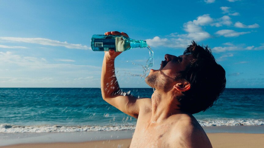 A man guzzles water from a bottle down at the beach