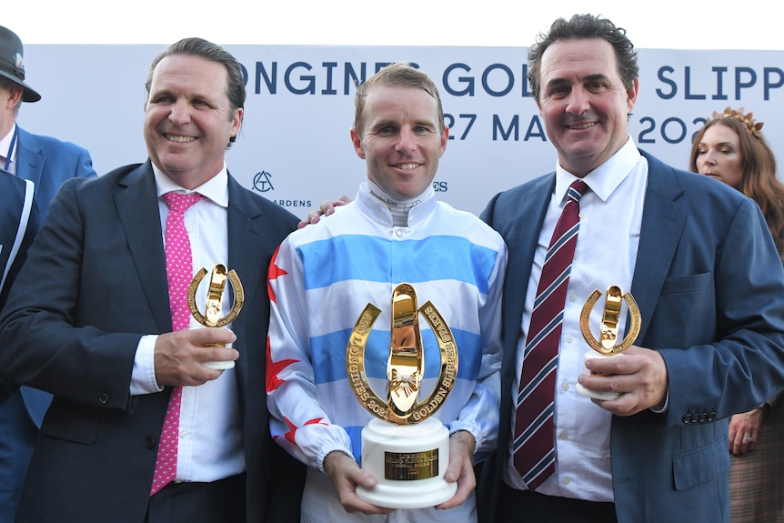 A jockey and two trainers stand with trophies after winning the Golden Slipper.