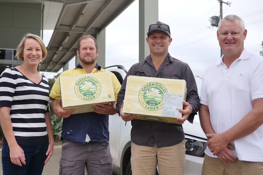 four people standing, two in the middle hold cartons of beer