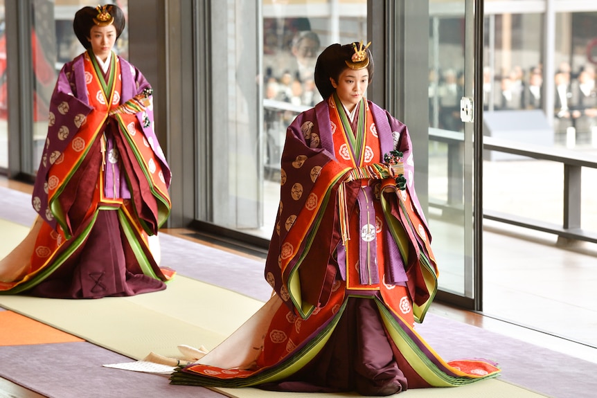 A woman in colourful robes looks down while walking along a white carpet 