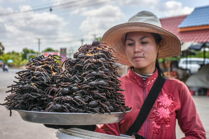 A Cambodian seller with a platter of spiders