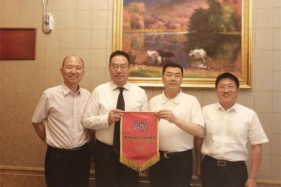 Li Fuxin holds a red banner while posing for a photo with three men in white shirts.