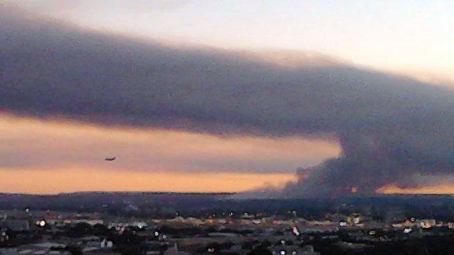 A plane lands at Sydney Airport as smoke from a burn-off fills the sky.