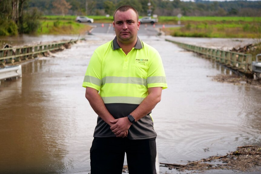 A man in high-vis stands in front of a flooded bridge.
