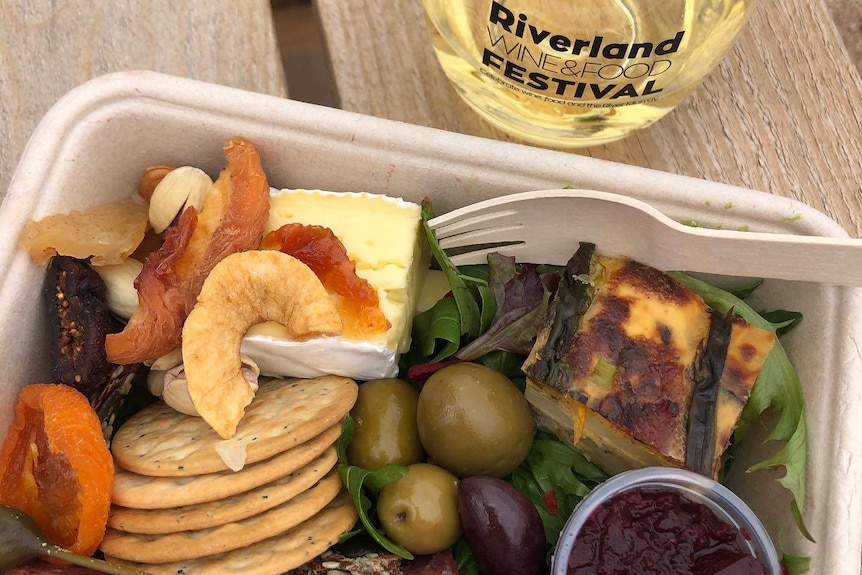 A container with salad, quiche, biscuits, cheese and dried fruit and a glass of a wine