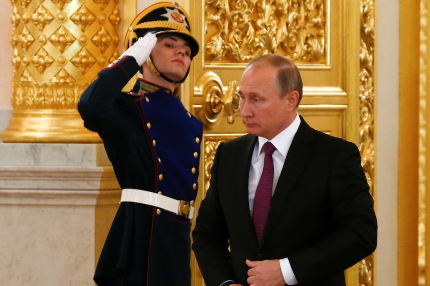 Vladimir Putin walks past a young man in military dress giving him a salute 