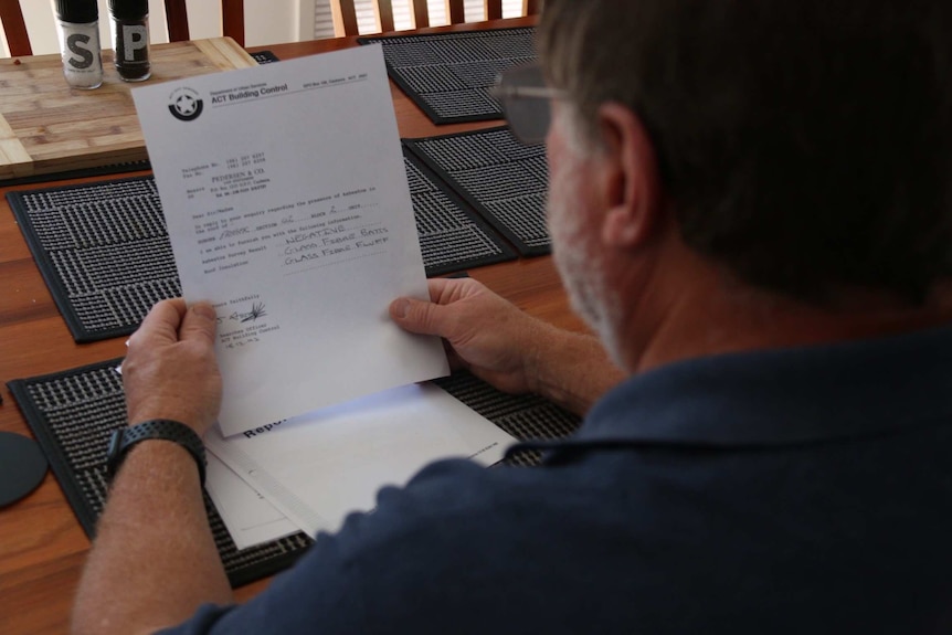 A man holds up a building report from the ACT Government.