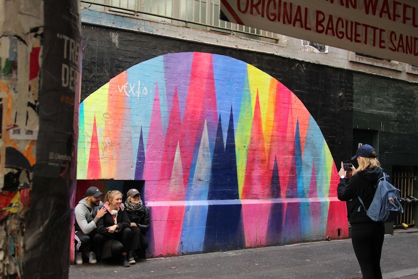 A woman takes a photo of three others in front of street art.