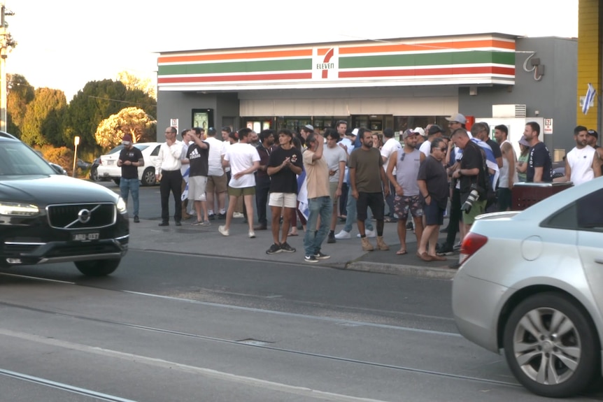 People gather outside a 711 on a budy Melbourne road.